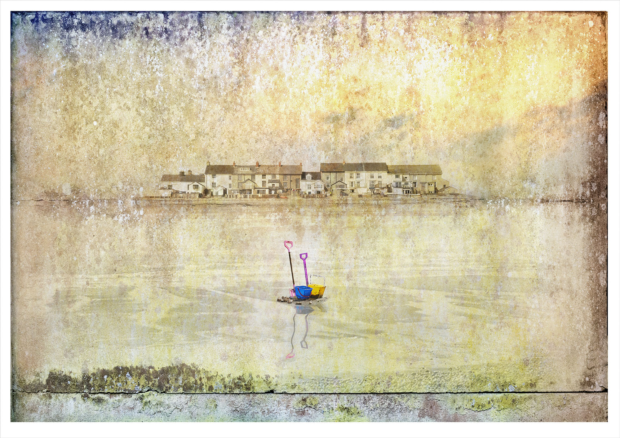 wet sand as if looking across an estuary to a row of distant houses. Childrens plastic bucket and spade in foreground